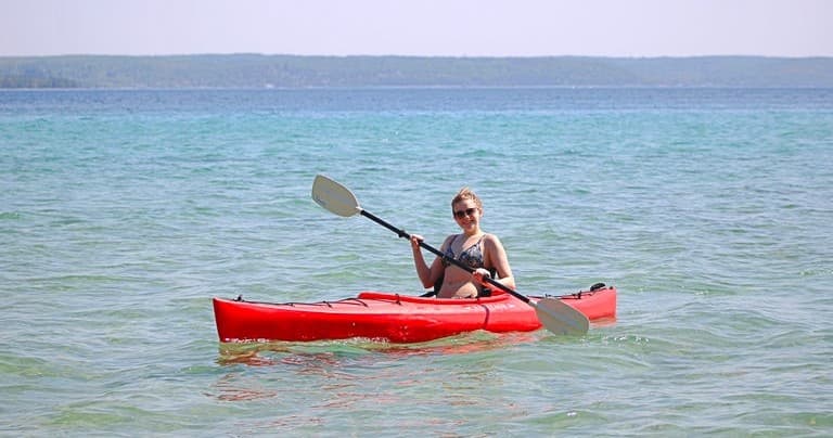 Solo kayaker paddling red kayak on clear coastal waters