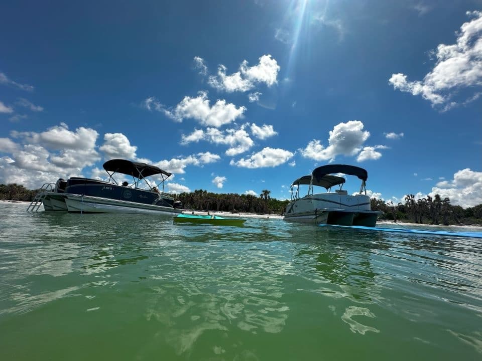 Two pontoon boats floating on calm emerald water under blue sky
