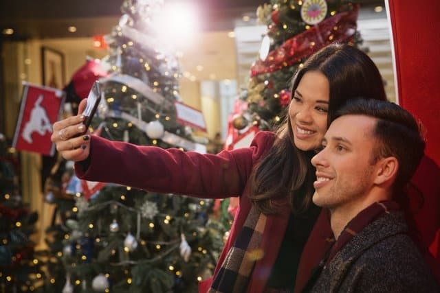 Couple taking holiday selfie by decorated Christmas market tree