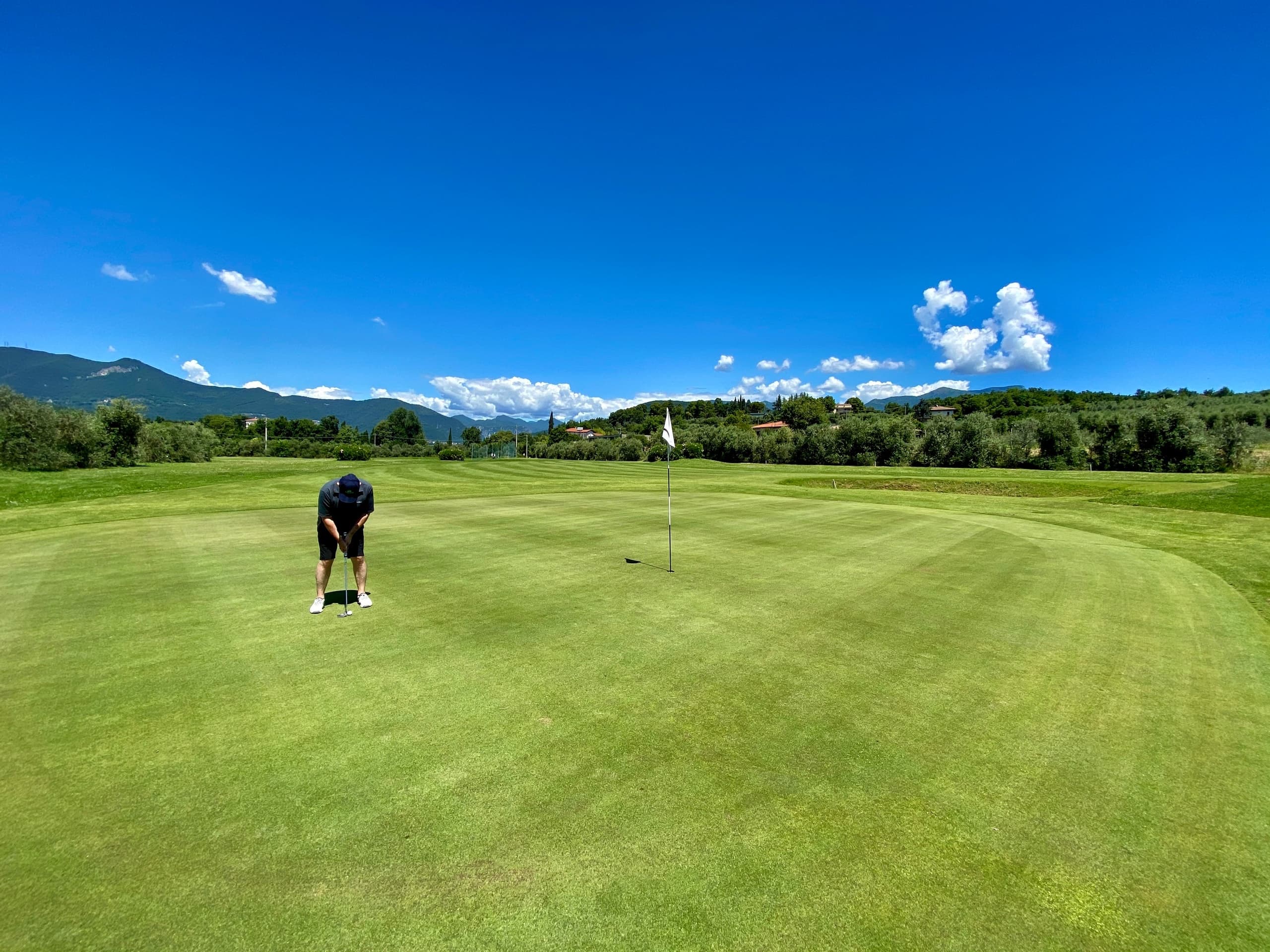 Golfer putting on green with expansive blue sky and mountains