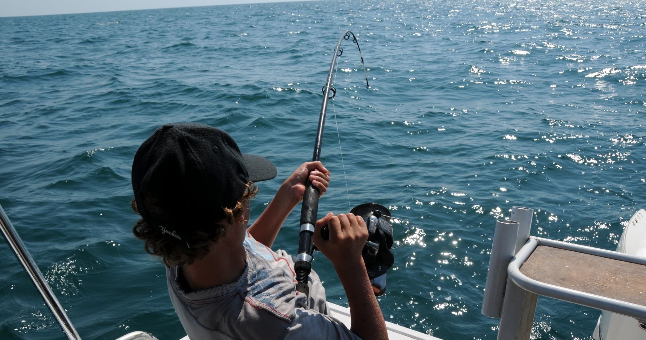 Youth angler reeling in catch on sportfishing boat in open sea