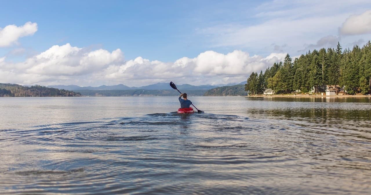Solo kayaker paddling on a calm lake with forested shoreline