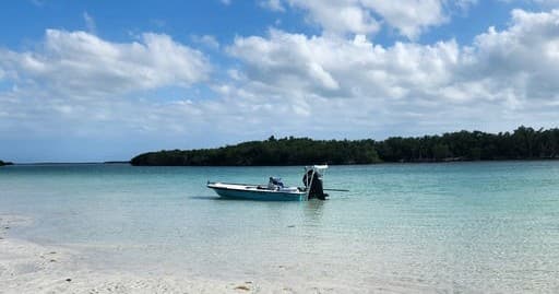 Skiff anchored in shallow turquoise bay off sandy tropical beach