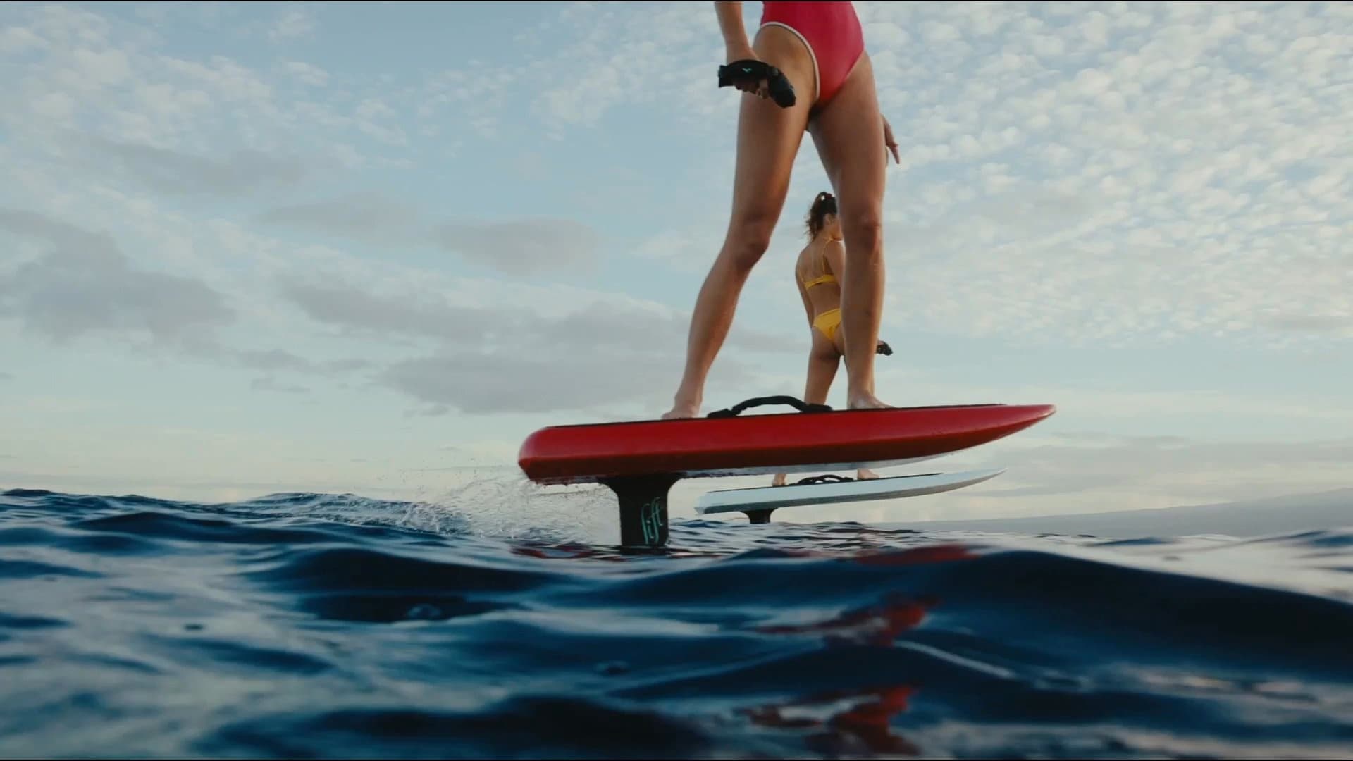 Rider on red e-foil gliding above ocean swells during sunrise