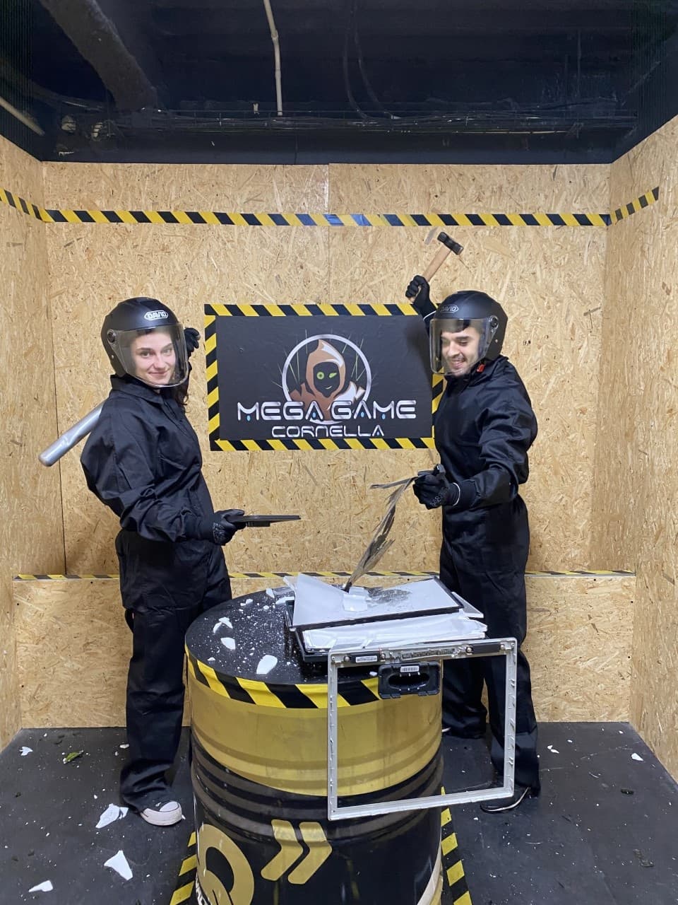 Two participants in protective suits smashing items in indoor rage room