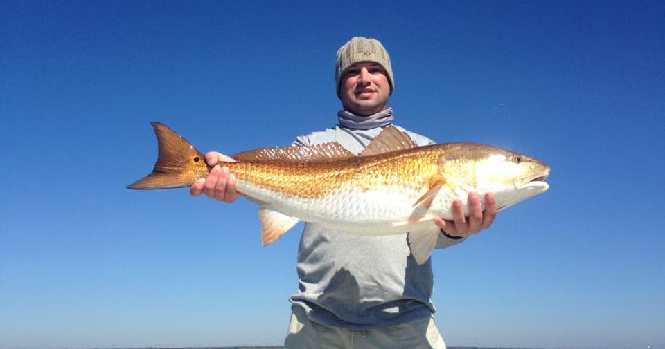 Angler holding large redfish on open ocean under blue sky