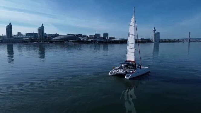 Small sailboat navigating calm harbor waters with skyline