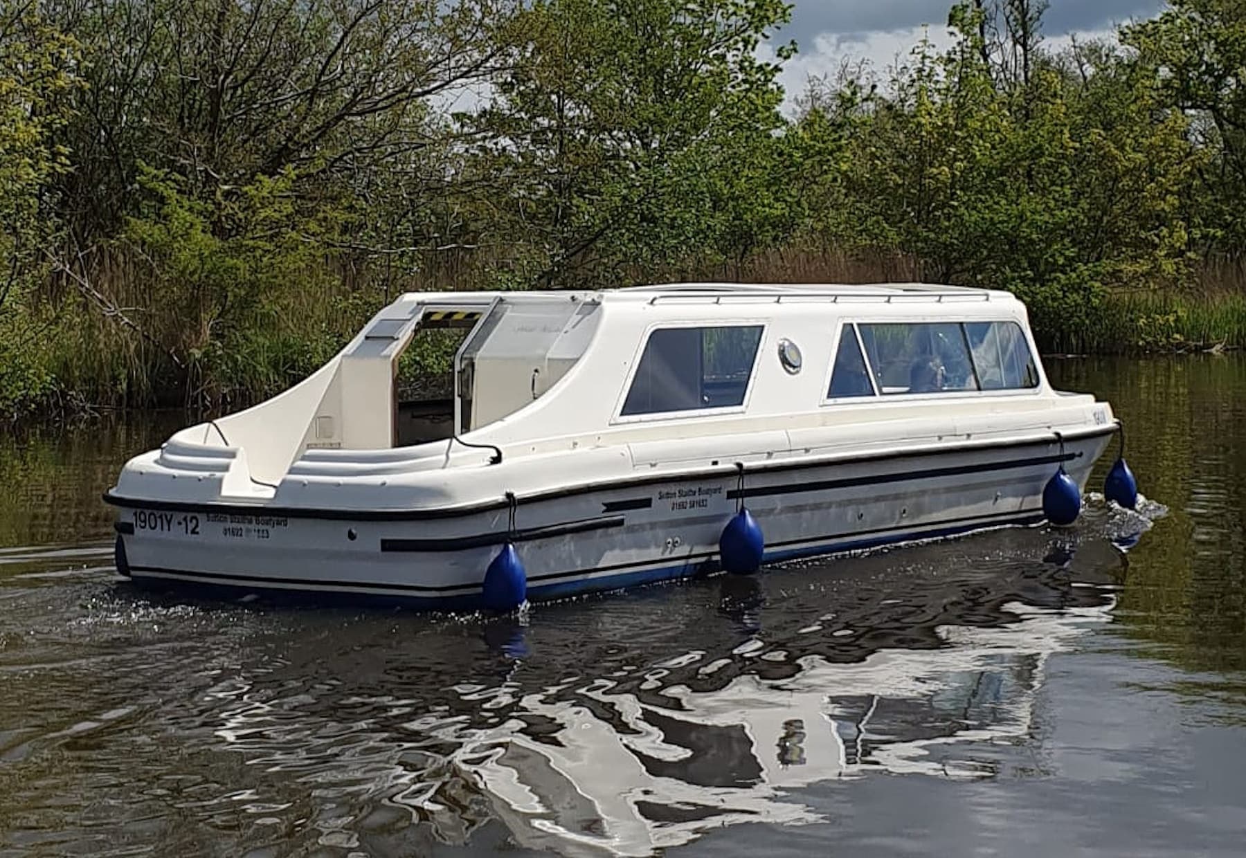 White cabin cruiser gliding along reed-lined riverbank