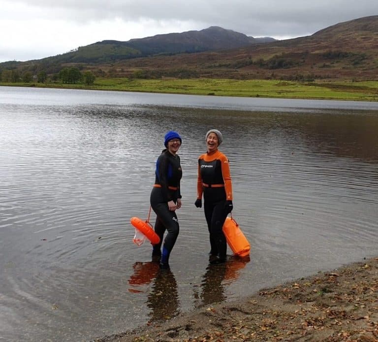 Two wetsuit swimmers on loch shoreline with orange safety buoys