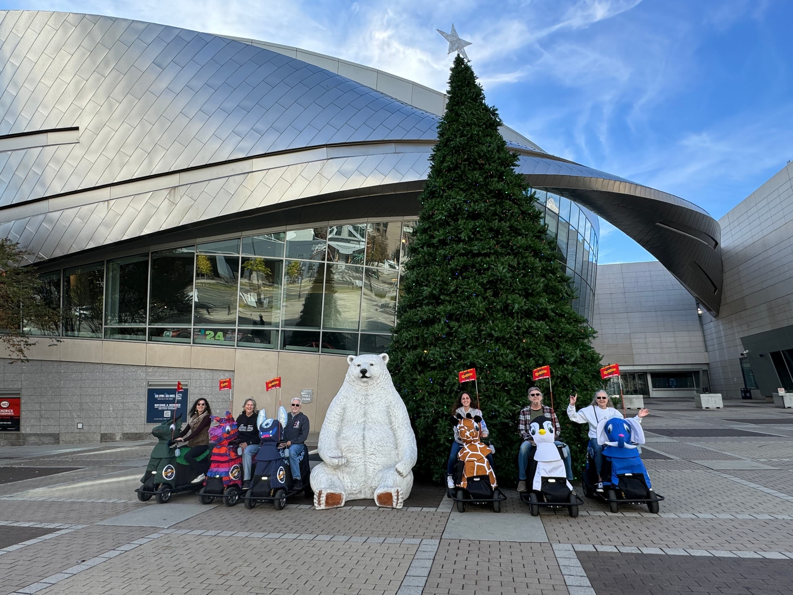 Group posing on mobility scooters by holiday tree at urban concert hall plaza