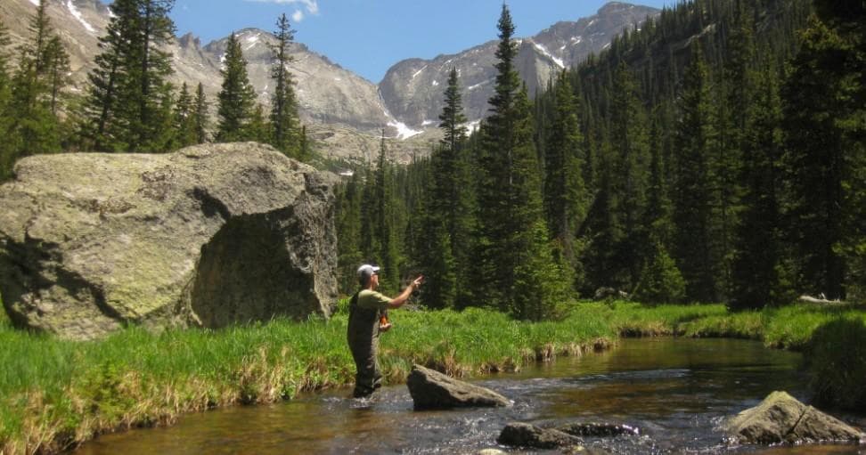 Fly angler casting on mountain stream with alpine peaks