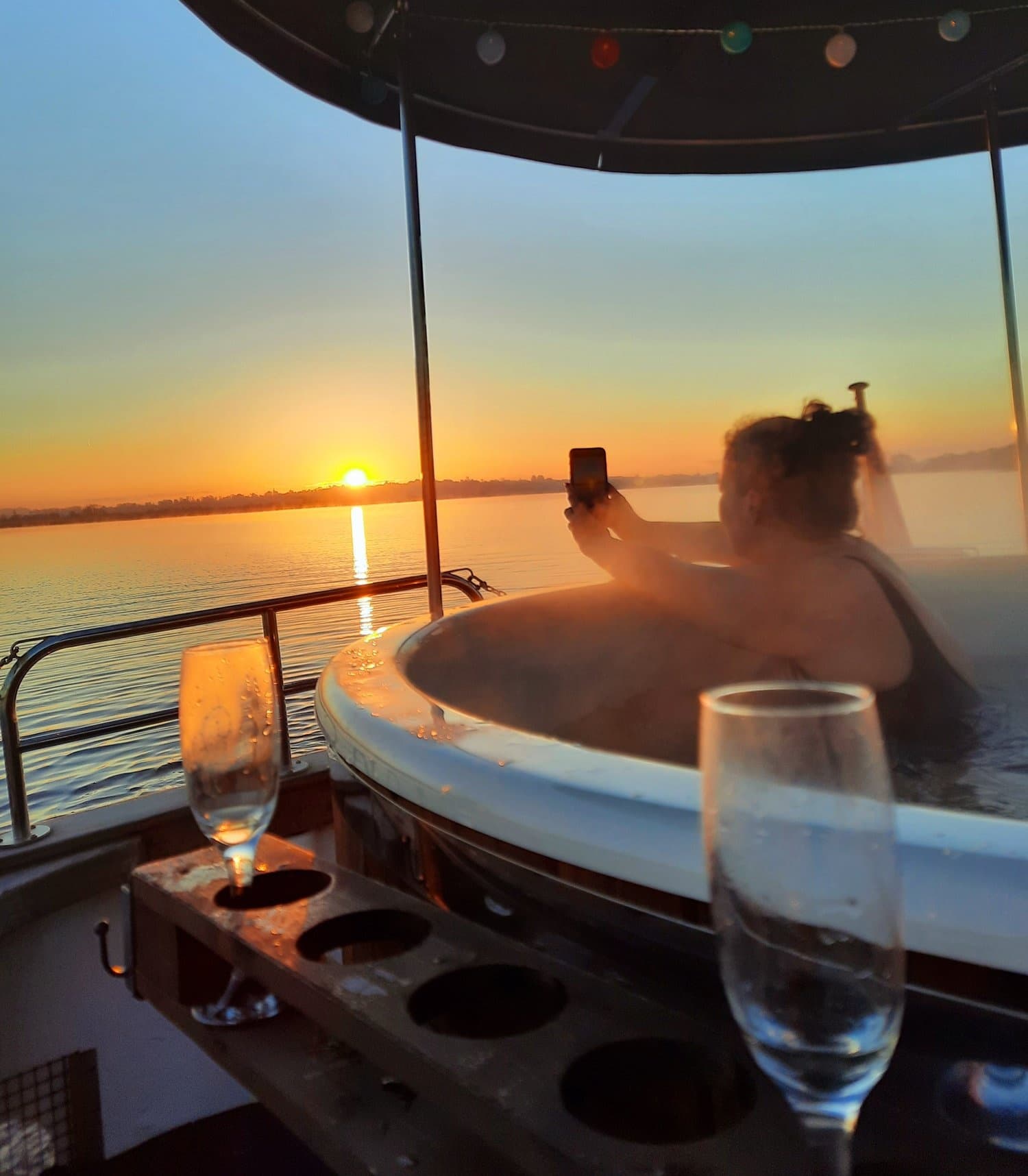 Guest enjoying boat hot tub at sunset, taking a phone photo