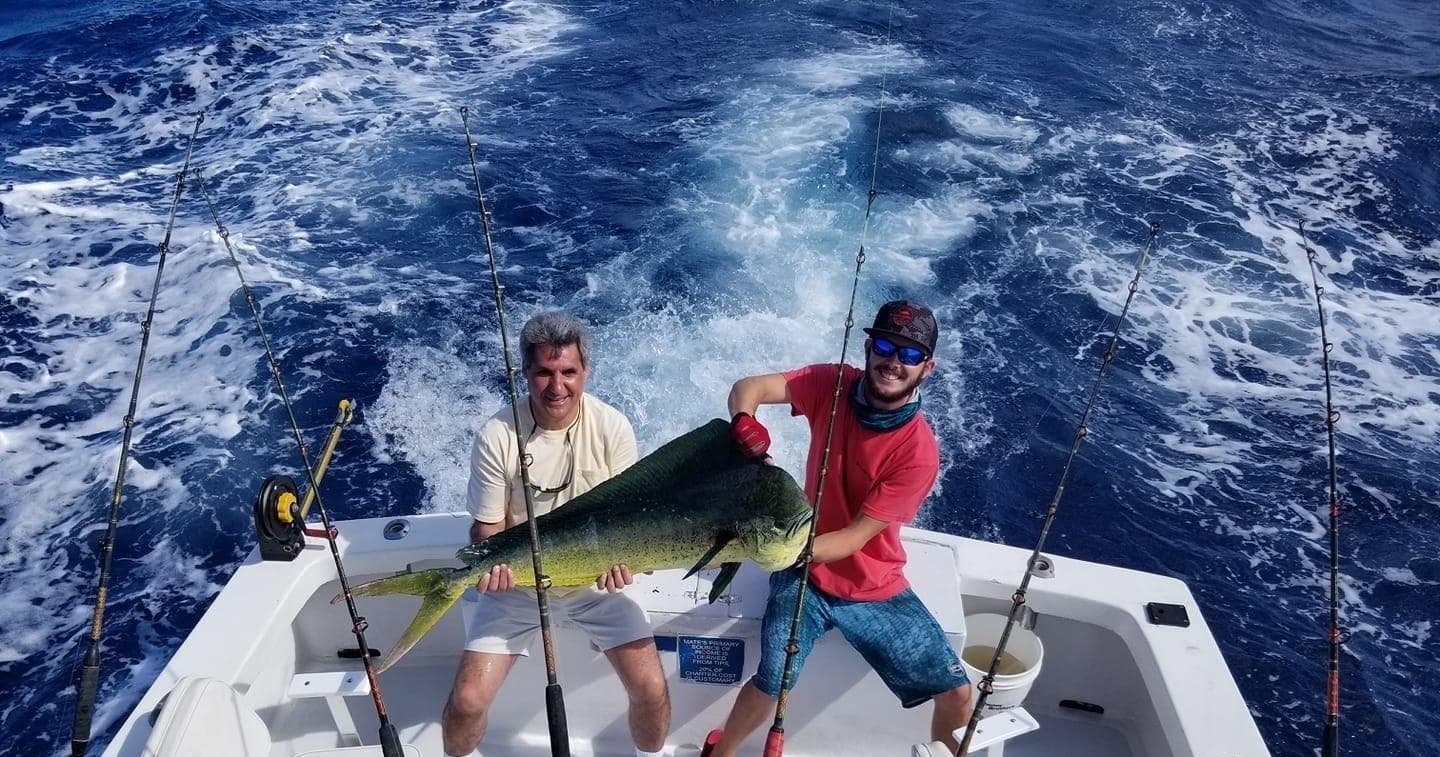 Anglers holding dolphinfish on sportfishing boat in deep blue ocean