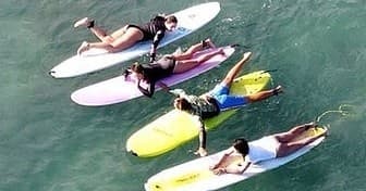 Group of five surf students lying on colorful boards in sea