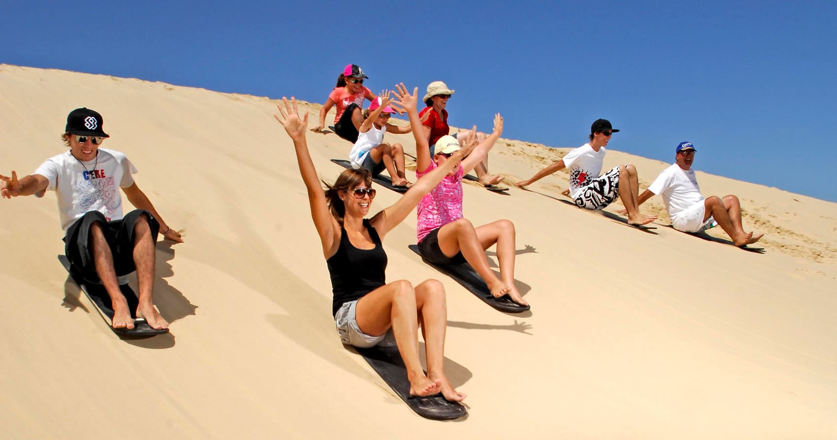 Group sandboarding and tobogganing on coastal dunes