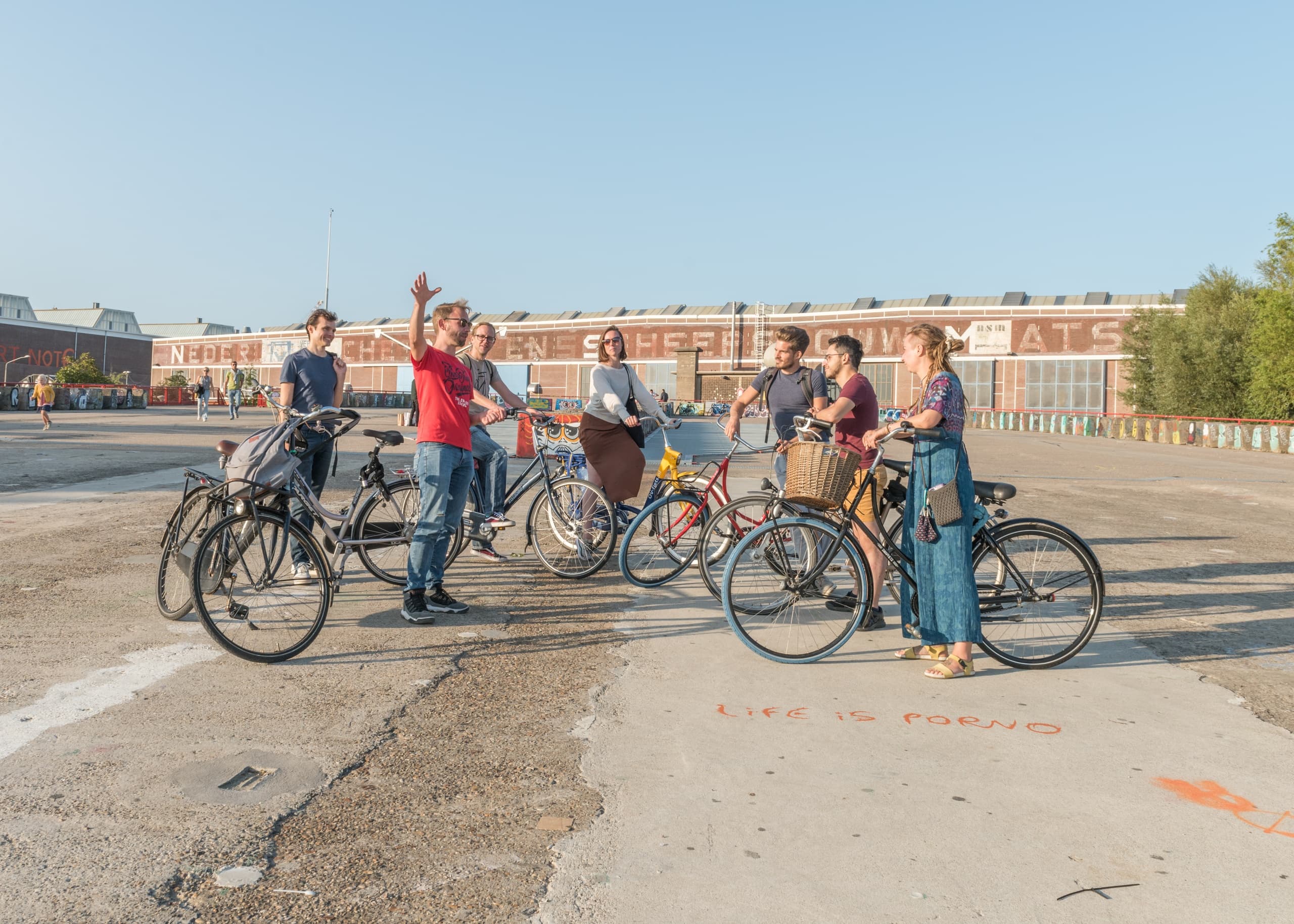 Urban bike tour group gathered in open plaza near warehouses