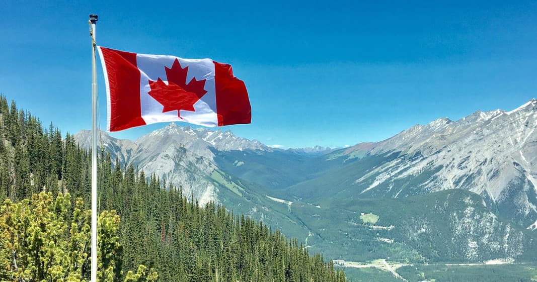 Canadian flag waving above mountain valley scenery in BC Rockies
