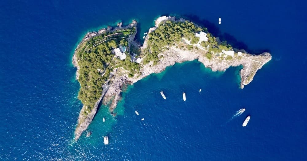 Aerial view of rocky island and moored boats in deep blue sea