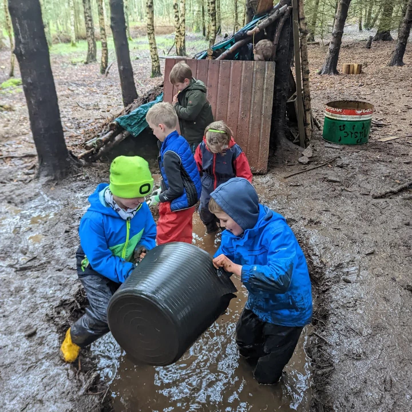 Kids carrying a barrel through muddy woodland during forest play