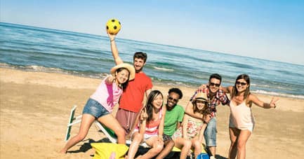 Friends posing on sunny beach with volleyball and ocean