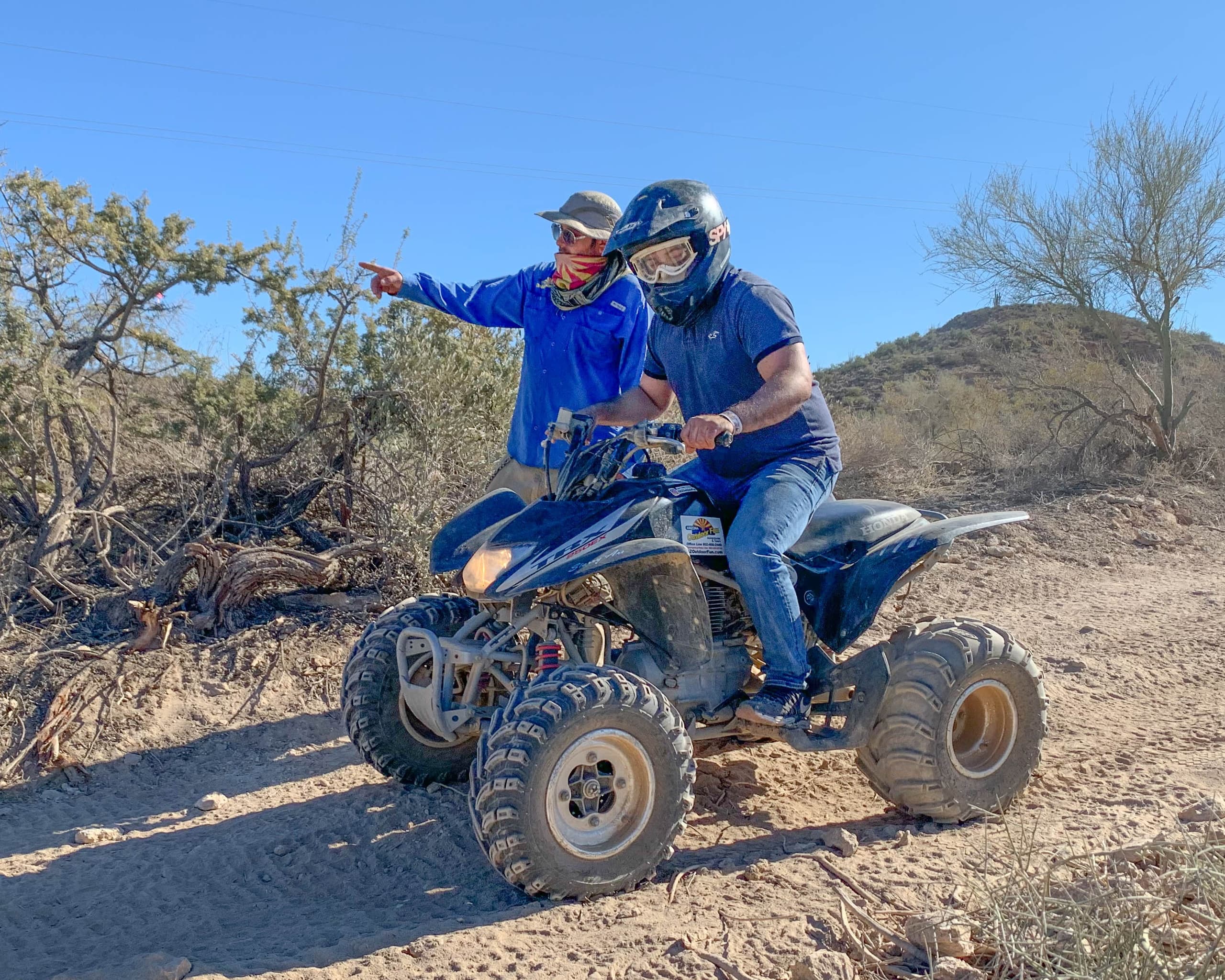 Two riders on ATV exploring rocky Arizona desert trail under sun