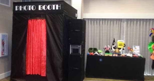 Black enclosed photo booth kiosk indoors with red curtain and props