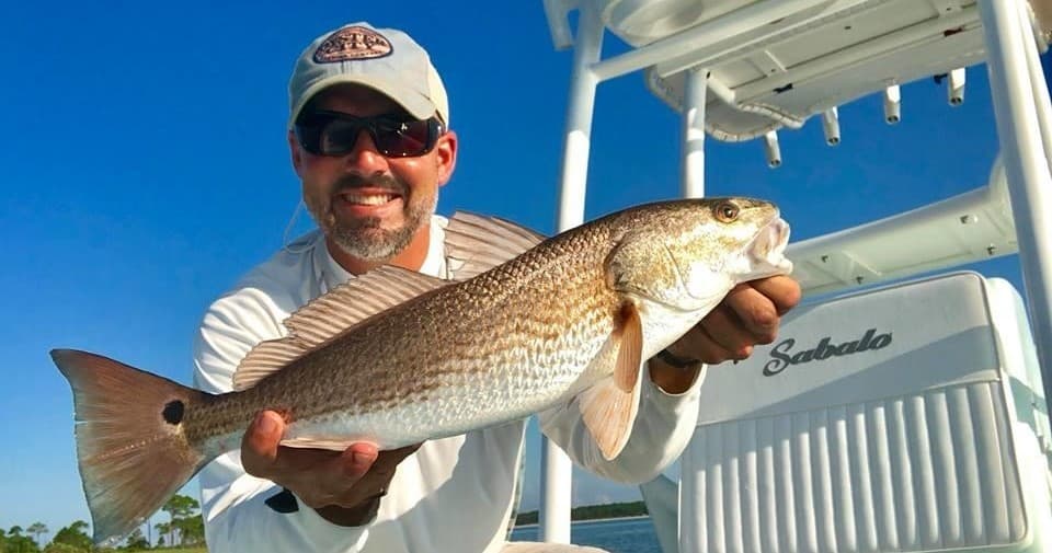 Angler holding redfish on charter boat in sunny gulf waters