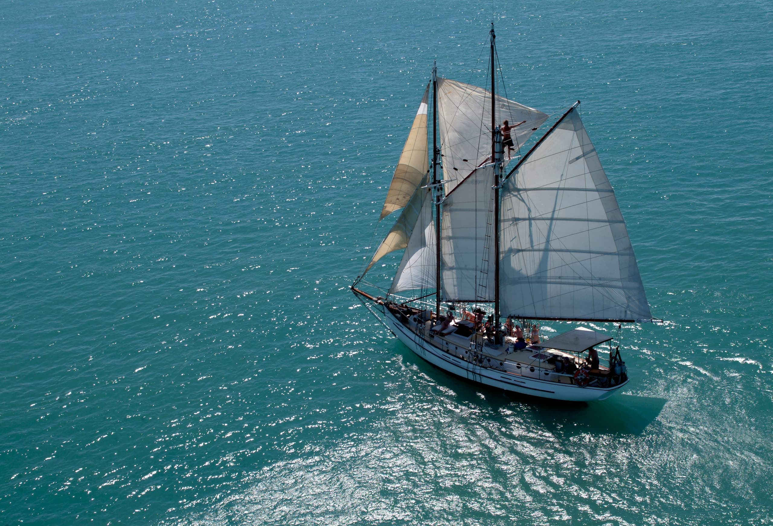 Aerial view of a tall-masted yacht sailing across blue ocean
