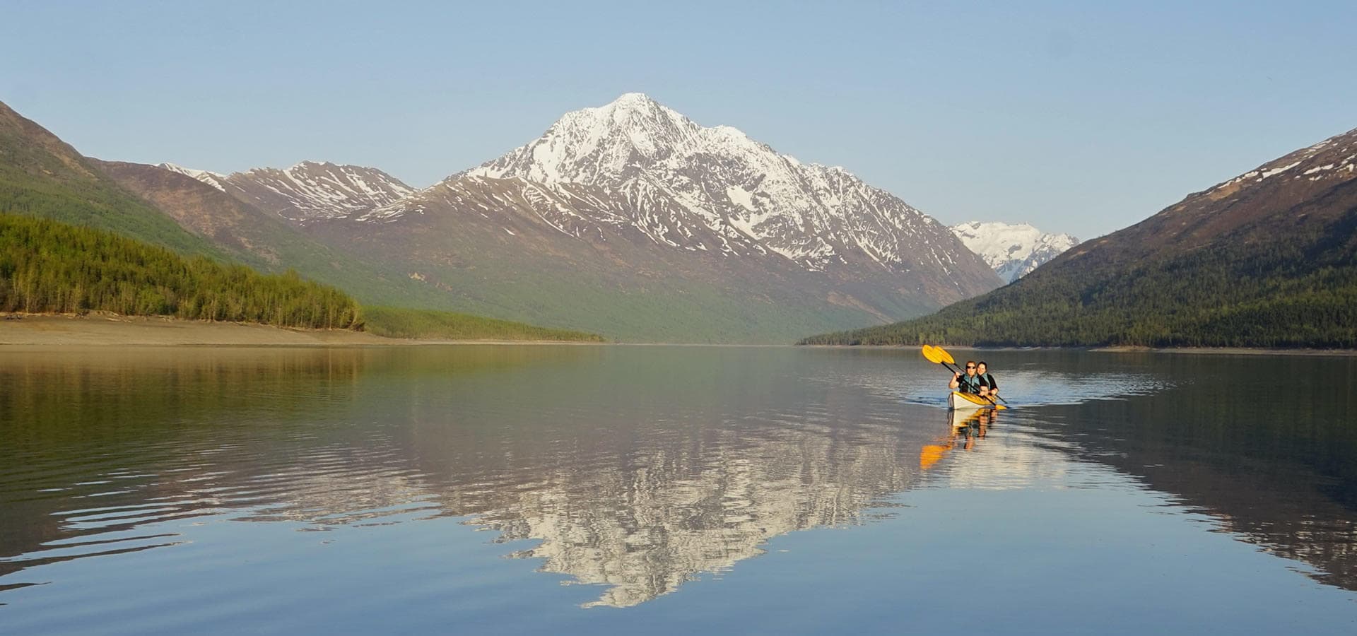 Solo kayaker paddling on glassy mountain lake with alpine reflection