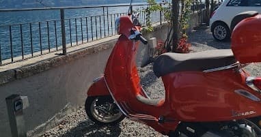 Red Vespa scooter parked by lakeside railing overlooking Lake Como