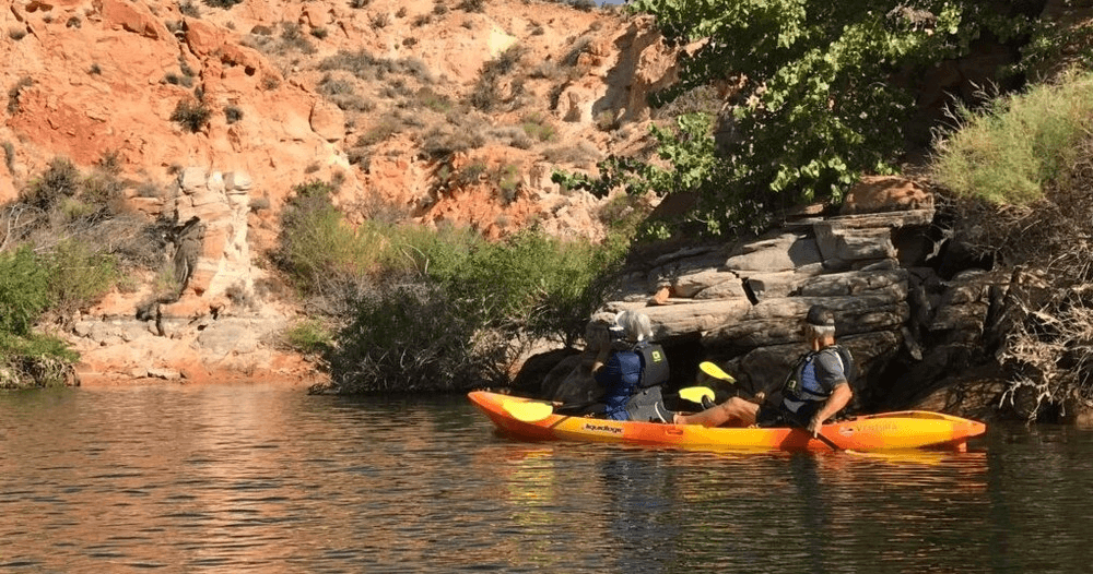 Two kayakers paddling near red rock canyon shoreline at midday