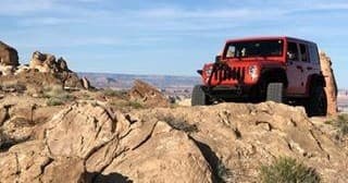 Red Jeep parked on rocky overlook with canyon vistas under blue sky