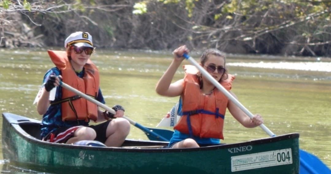 Two paddlers canoeing on a slow river wearing lifejackets