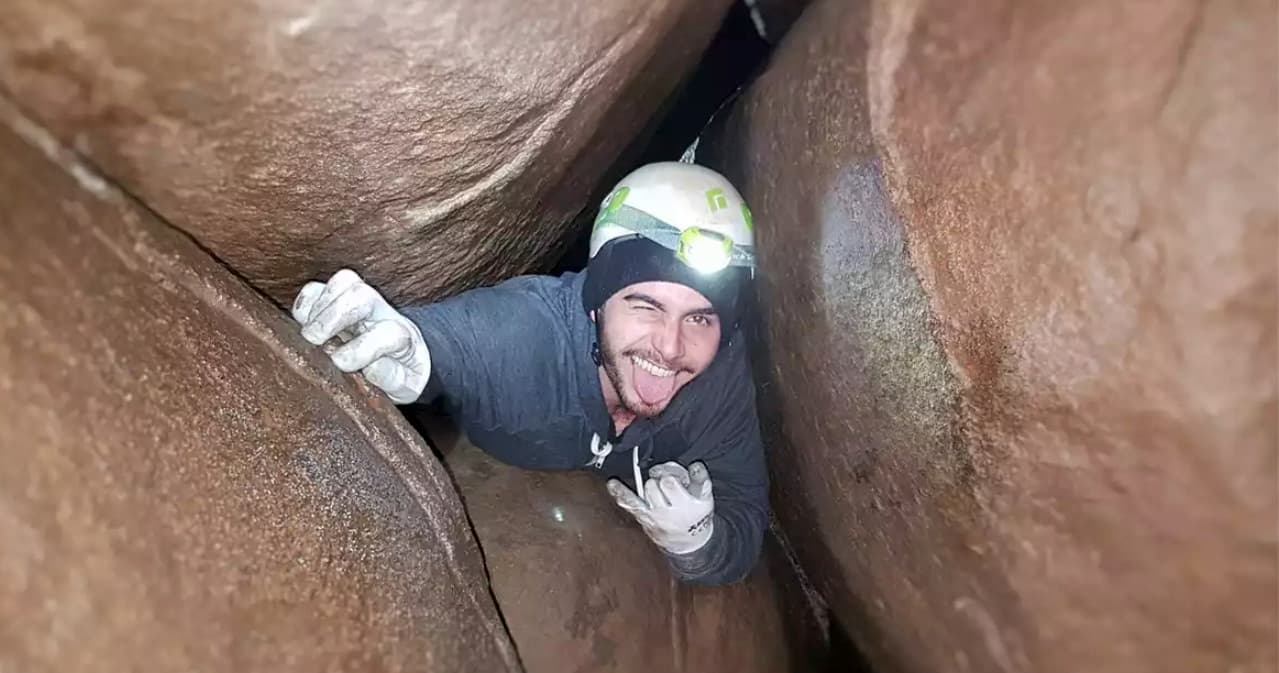 Caver squeezing through narrow slot canyon passage with helmet