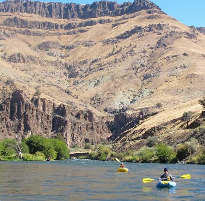 Kayakers paddling calm river beneath arid canyon cliffs