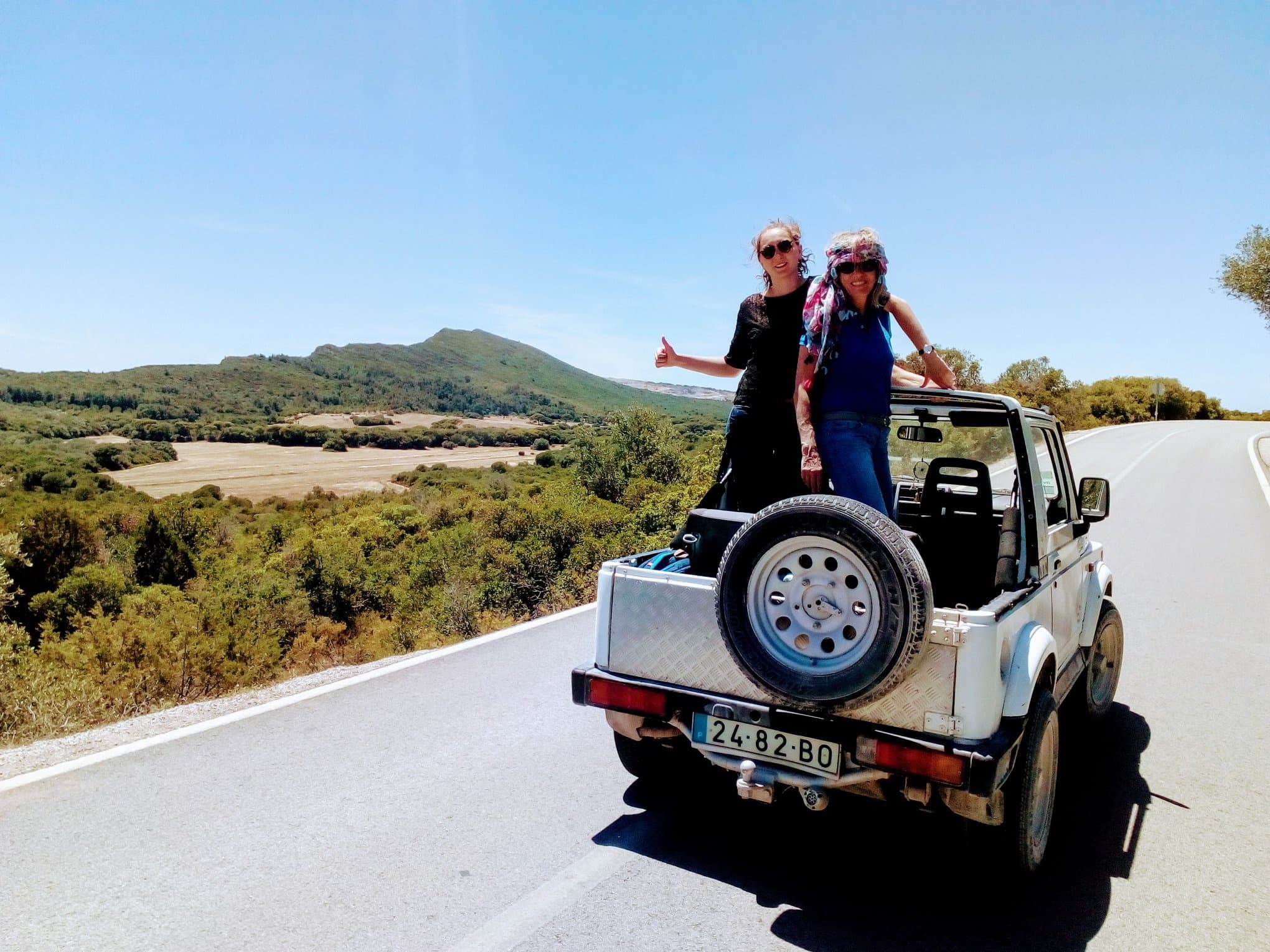 Couple standing on open-top jeep enjoying scenic country drive