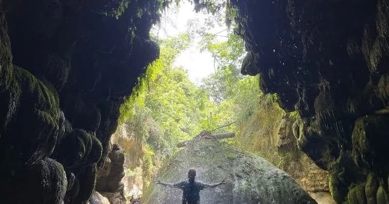 Hiker exploring mossy cave opening into a tropical forest gorge