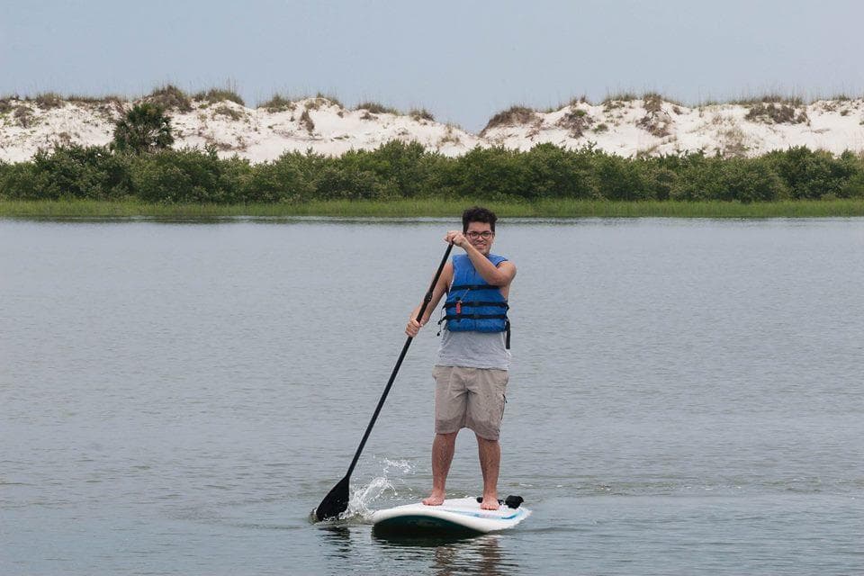 Man paddling on SUP in shallow bay near dunes, calm water