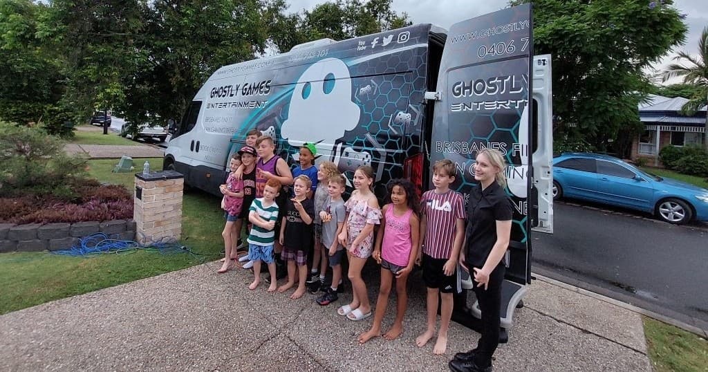 Group of kids posing by GhostlyGames van at suburban driveway event
