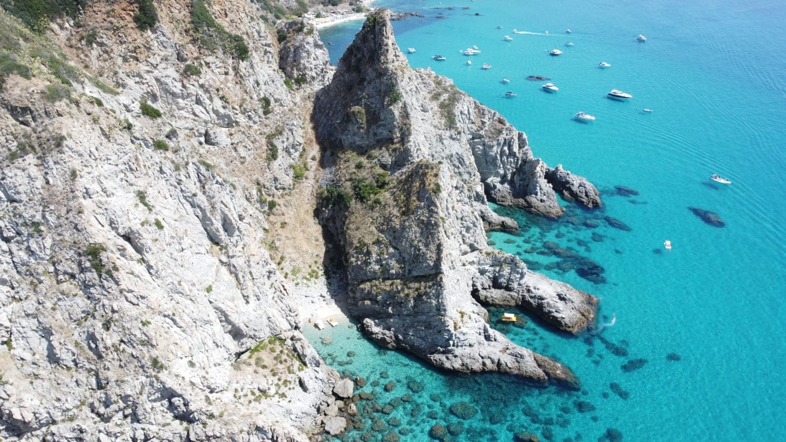 Aerial rock promontory and turquoise cove with anchored boats