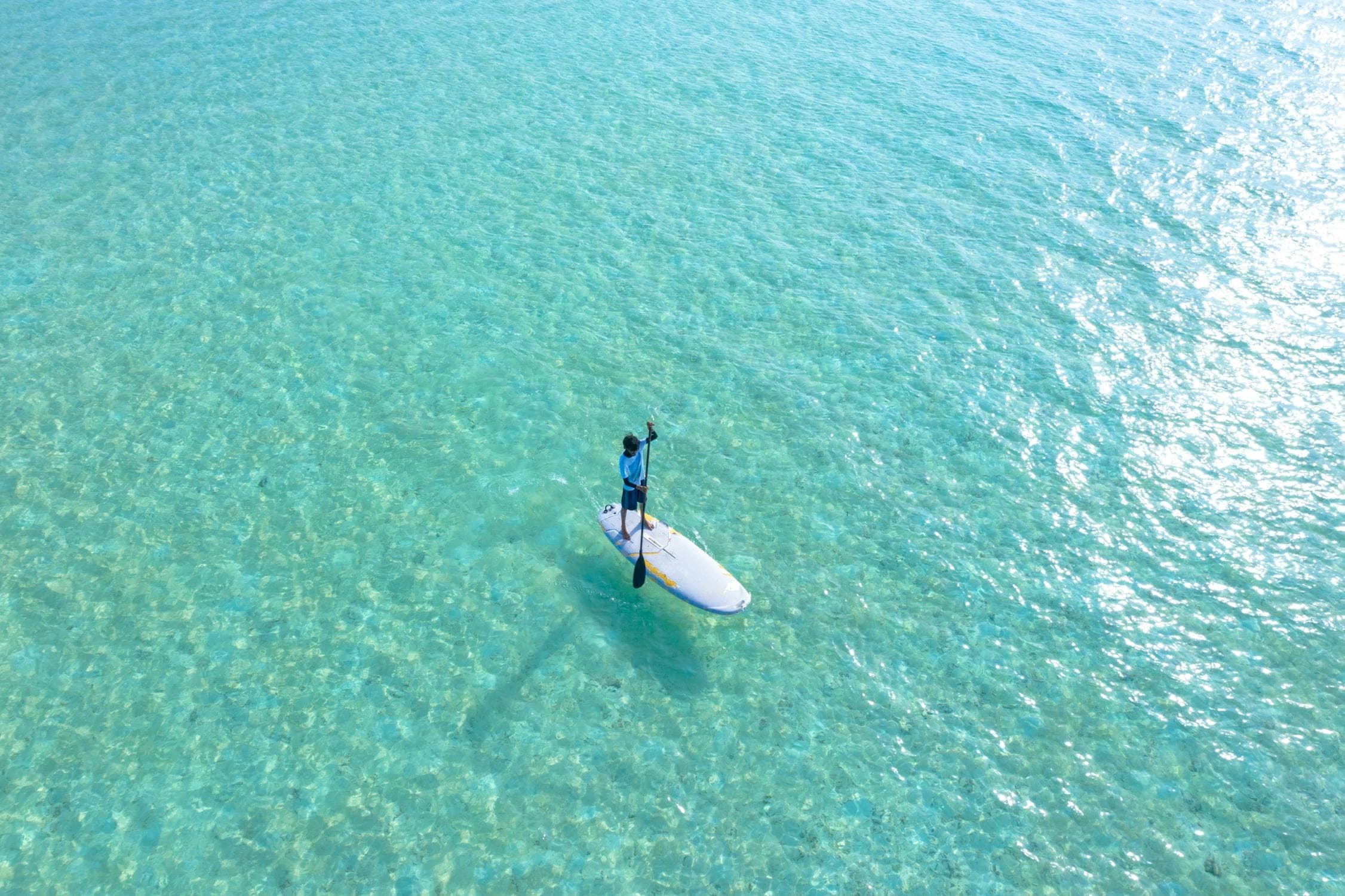 Stand-up paddleboarder drifting on turquoise shallow ocean