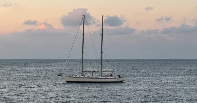 Twin-mast sailboat anchored offshore at sunset over calm sea