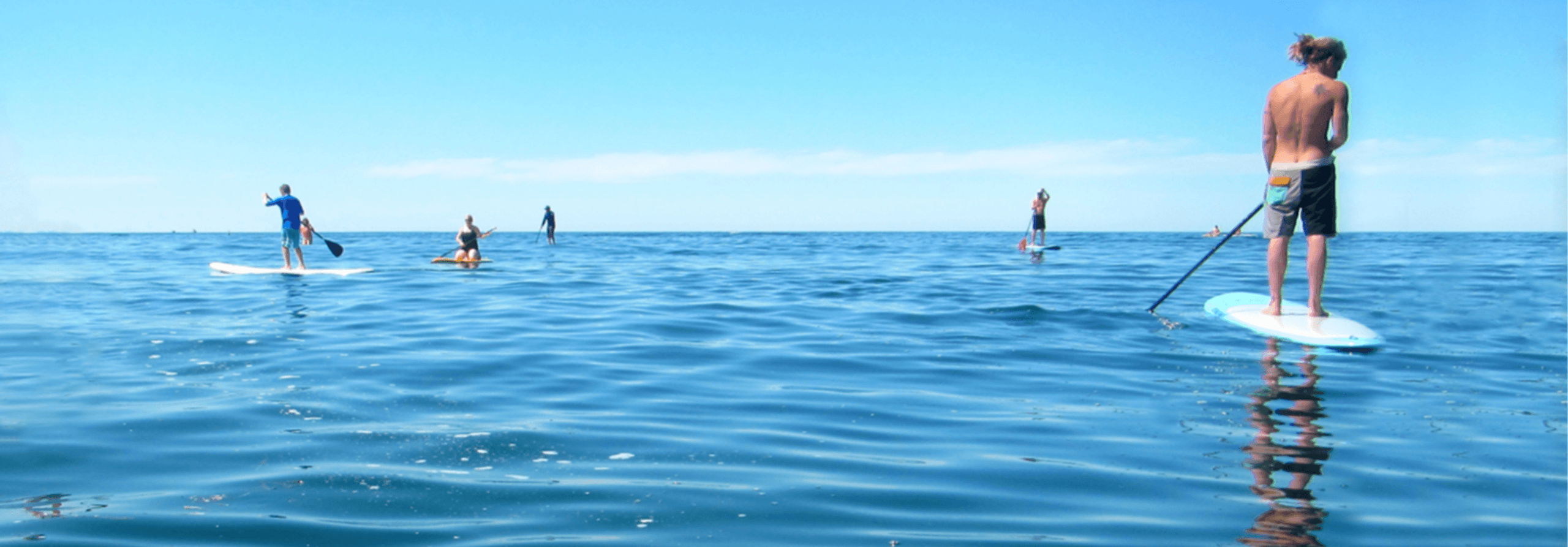 Paddleboarders on calm open ocean under clear blue sky