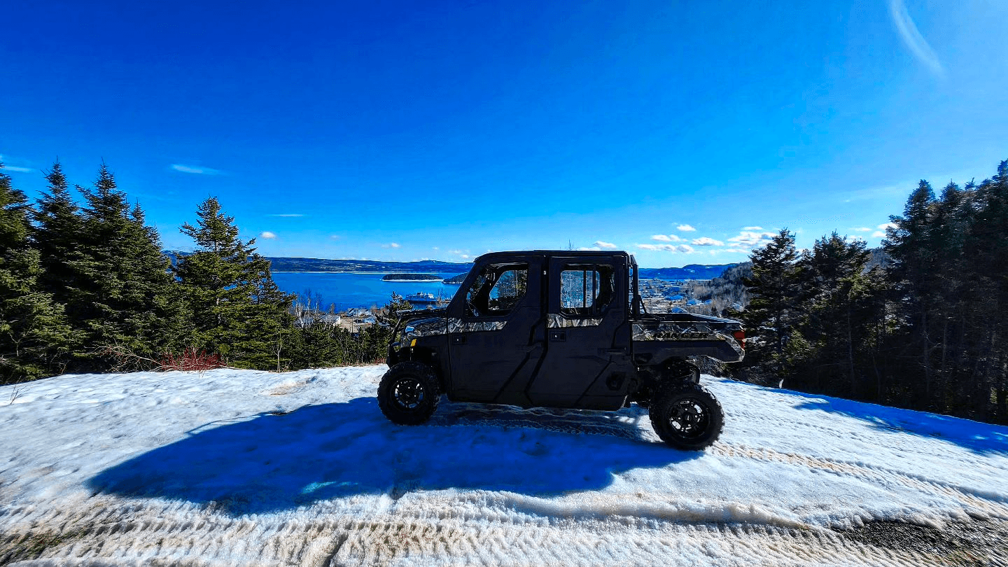 Side-by-side UTV parked on snowy overlook with ocean view