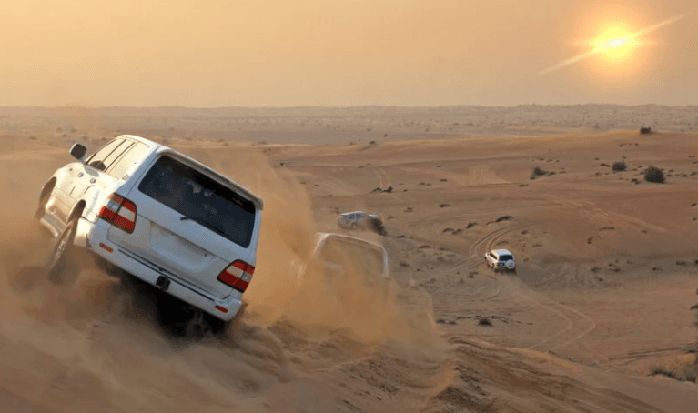 SUVs dune bashing across desert dunes at sunset in Arabian desert