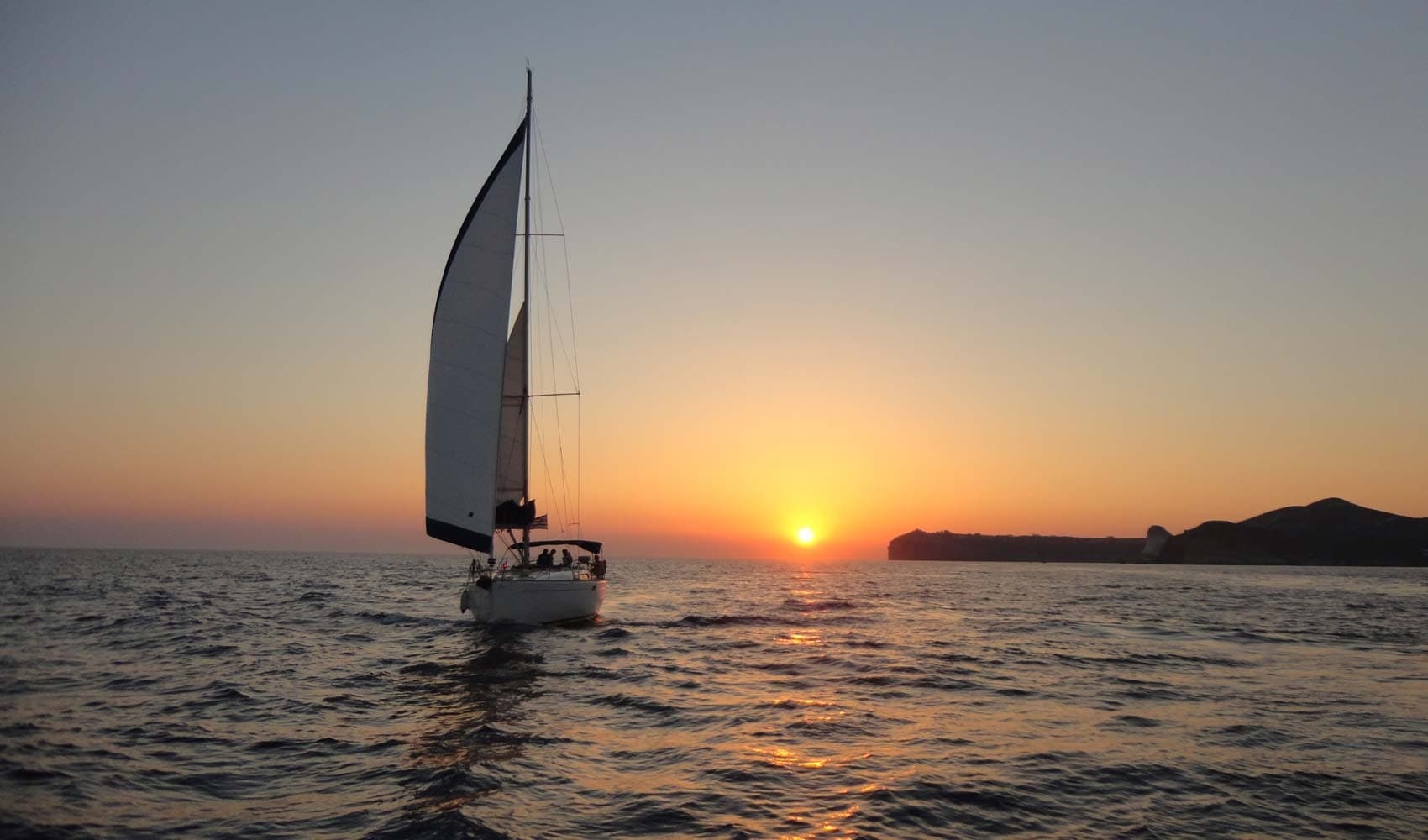 Sailboat silhouetted at sunset over open ocean horizon