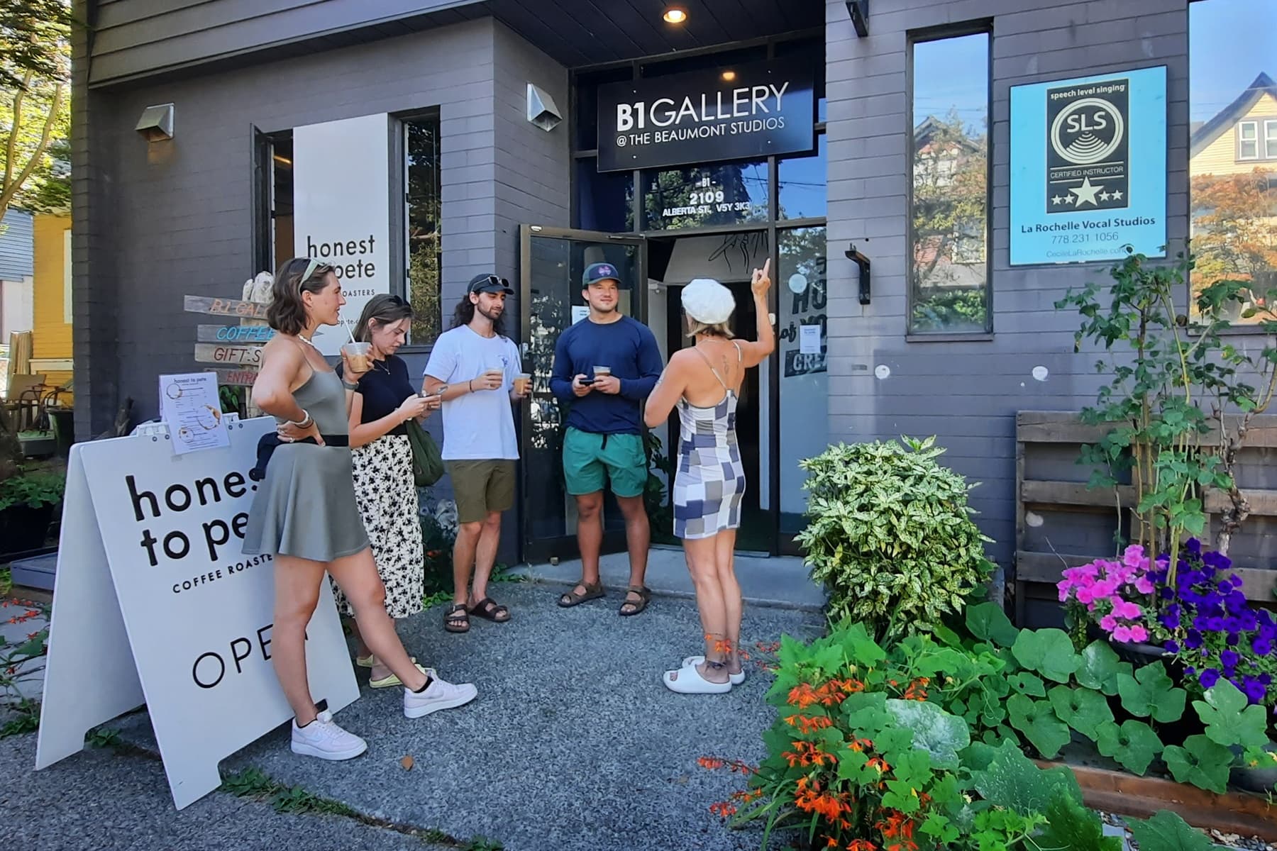 Visitors chatting outside small art gallery storefront with garden