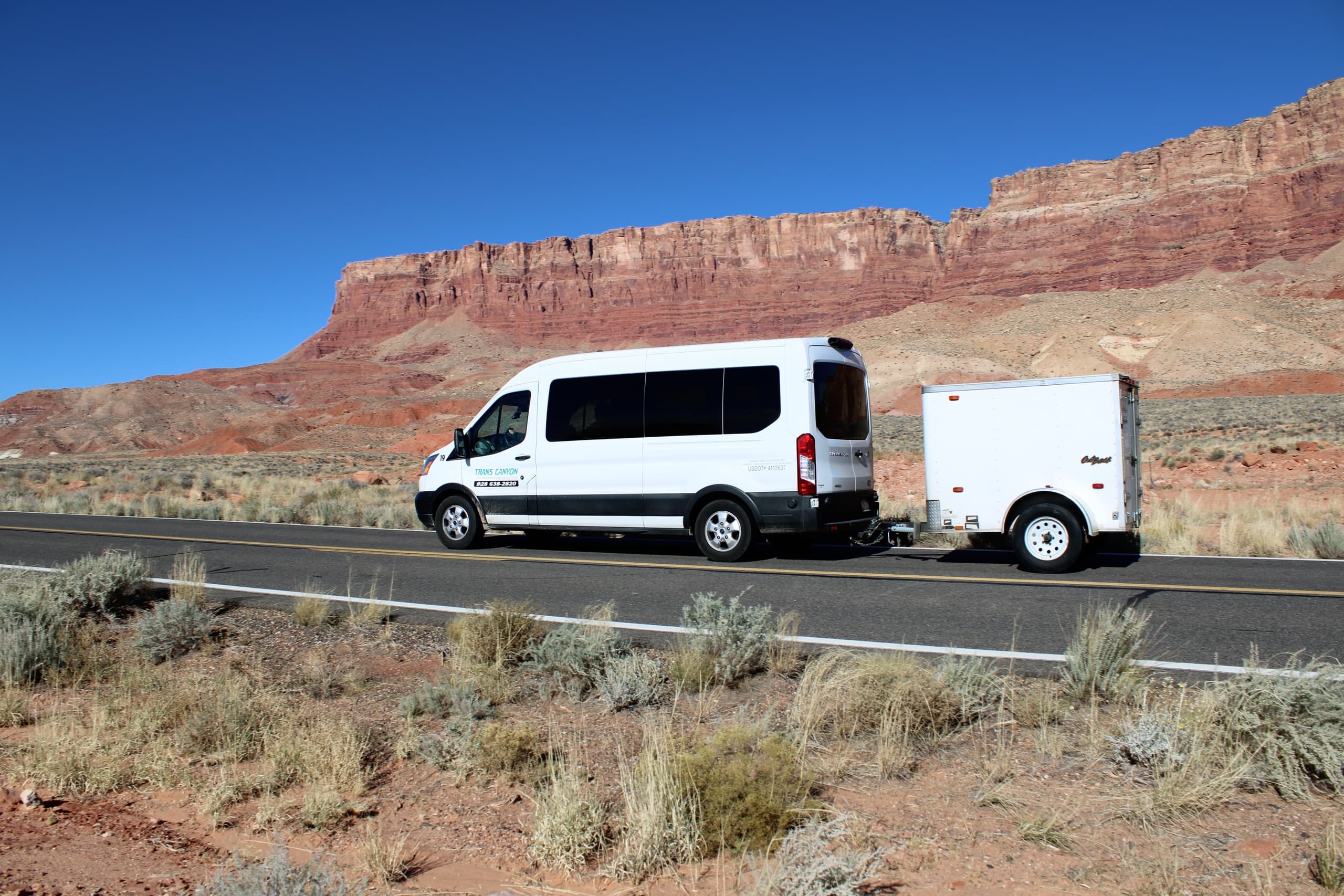 Tour van and trailer driving past red rock desert landscape