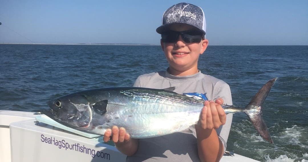 Young angler holding tuna aboard charter boat on calm sea