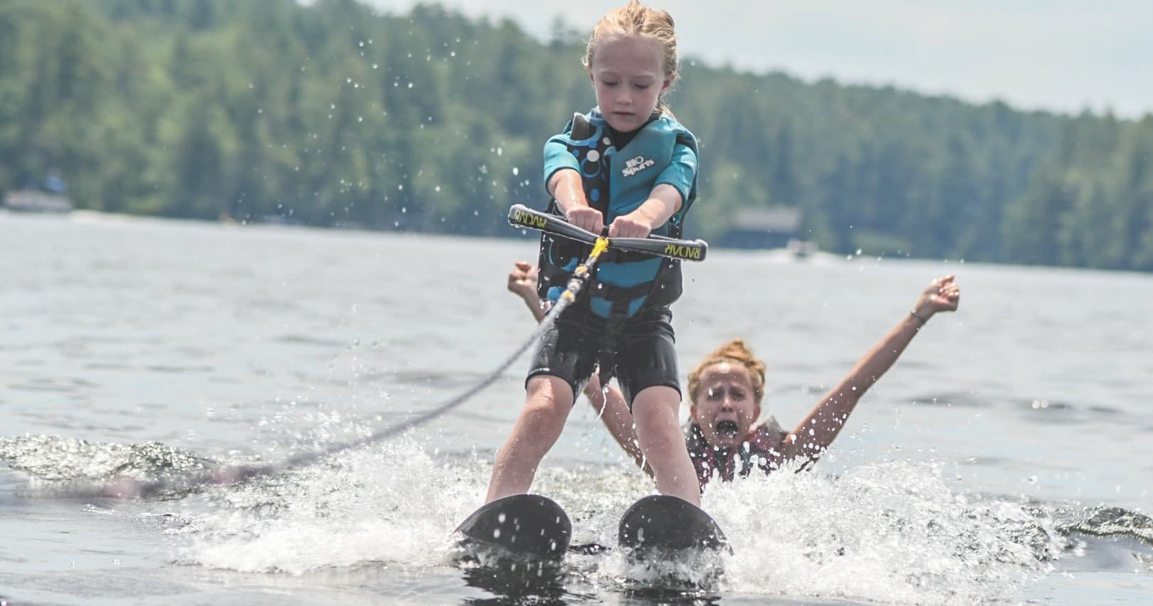 Child waterskiing tandem with instructor on calm lake